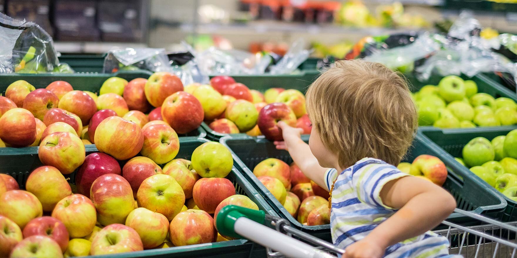 Junge im Einkaufskorb greift im Supermarkt nach Apfel
