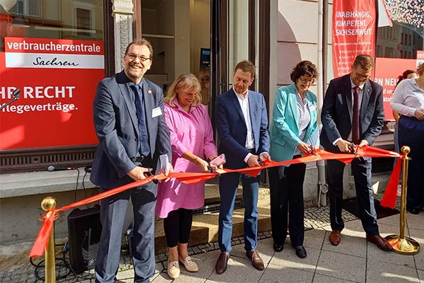 5 Personen stehen vor einem Gebäude und halten gemeinsam ein rotes Band in den Händen